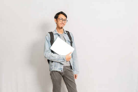 A male with his folded laptop standing isolated in front of white background. Indonesian or southeast asian model.