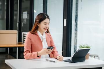 Young beautiful woman typing on tablet and laptop while sitting at the working white table modern office..