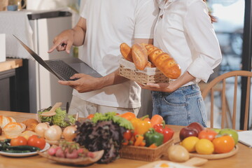 Handsome man sitting near his wife at kitchen. Family couple see social media, surf the web while sitting at kitchen table with generic laptop. Couple working with laptop at home