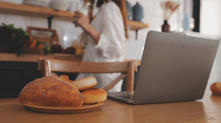 Portrait of pretty freelancer female working typing on laptop computer sitting at table smiling looking to screen in kitchen. Attractive redhead young woman remote working on laptop from home office.