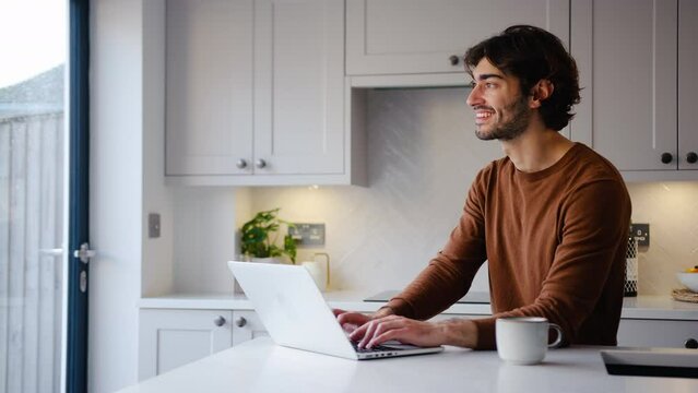 Young man working from home on laptop sitting at kitchen counter - shot in slow motion