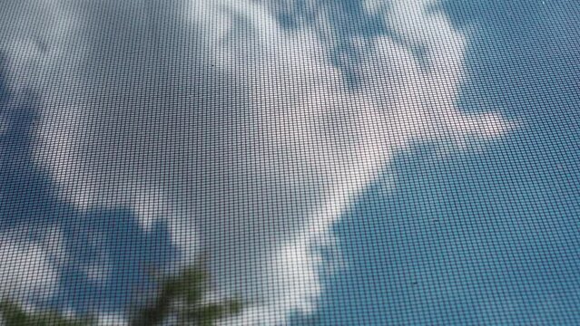 Blue sky with clouds through a protective mosquito net.