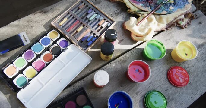 Close up of paints and brushes on table in sunny garden, slow motion