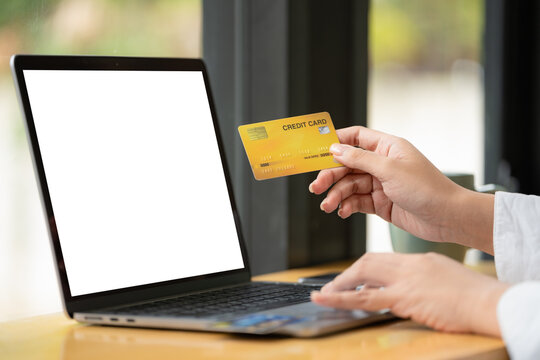 Mockup image of a woman holding credit card while using laptop with blank white screen.
