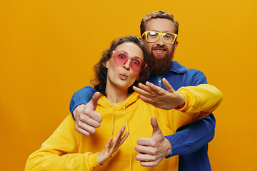 Obraz premium Man and woman couple smiling cheerfully and crooked with glasses, on yellow background, symbols signs and hand gestures, family shoot, newlyweds.
