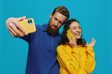 Woman and man funny couple with phones in hand taking selfies crooked smile fun, on blue background. The concept of real family relationships, talking on the phone, work online.