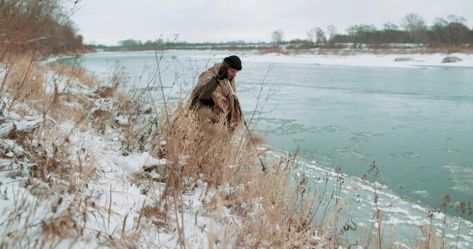 Nordic walking Active man hicker working out outdoor walks along bank of river with flowing ice Man trains body, engaged in health Sport walking adventure and exercising for hiking with poles outdoors