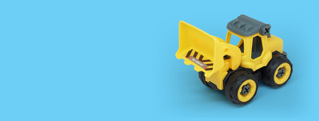 Naklejka premium yellow plastic bulldozer toy isolated on blue background with copy space for toy store banner