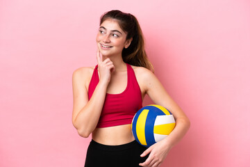 Young caucasian woman playing volleyball isolated on pink background thinking an idea while looking...