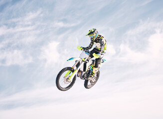 Naklejka premium Blue sky, jump and man on motorbike in air for practice, training and extreme sports energy. Professional dirt biking speed challenge, off road adventure and danger at off road motorcycle competition
