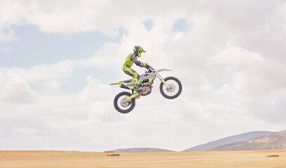 Fototapeta na wymiar Desert, motorbike cycling and jump for sports, agile driving and off road adventure with mockup space in cloudy sky. Motorcycle, challenge and moving in air for action, fearless talent and sand dunes