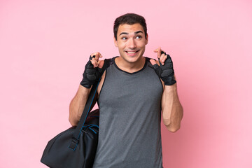 Young sport caucasian man with sport bag isolated on pink background with fingers crossing