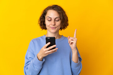 Young English woman isolated on pink background using mobile phone and lifting finger