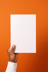 A human hand holding a blank sheet of white paper or card isolated on orange background