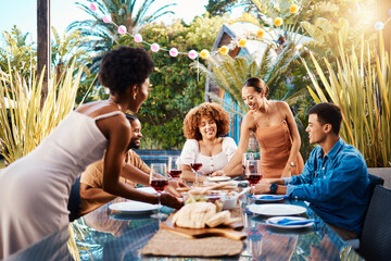 Friends, outdoor and eating food at a table for social gathering, happiness and holiday celebration. Diversity, men and women group at lunch, party or reunion with wine in a garden for fun and relax
