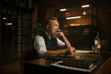 Pensive senior business man smoking cigar while sitting at work table