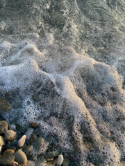photograph of sea foam on the seashore pebbles close up