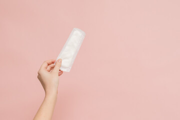 Woman's hand holding sanitary pad on pink background
