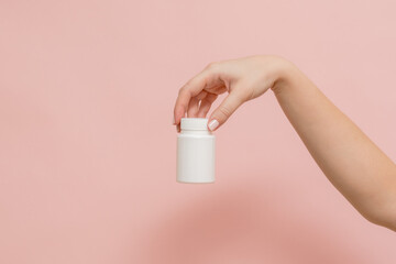 Plastic bottle (tube) in hand on pink background. Packaging for vitamins, tablets or capsule, or supplement