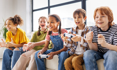 Group of joyful teenage friends with joysticks enthusiastically playing game console  . - 636579986
