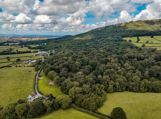 Drone birdseye shot of a dense green forest of trees and hill in english countryside with fields