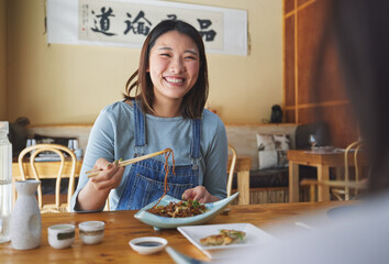 Japanese, food and woman at a restaurant eating for dinner or lunch meal using chopsticks and feeling happy with smile. Plate, date and person enjoy Asian cuisine, noodles or diet at a table