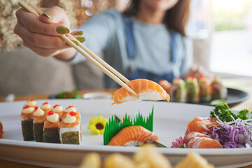 Hands, chopsticks and woman with sushi in restaurant, fine dining and eating in cafe store. Salmon,...