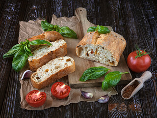 Freshly baked pieces of ciabatta with sun-dried tomatoes, fresh tomatoes, green basil leaves, garlic and spices. Composition on a dark wooden background.