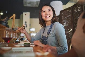 Foto auf Acrylglas Asian, sushi and woman at a restaurant eating for dinner or lunch meal using chopsticks and feeling happy with smile. Plate, young and person enjoy Japanese cuisine, noodles or diet at a table © Azee Jacobs/peopleimages.com