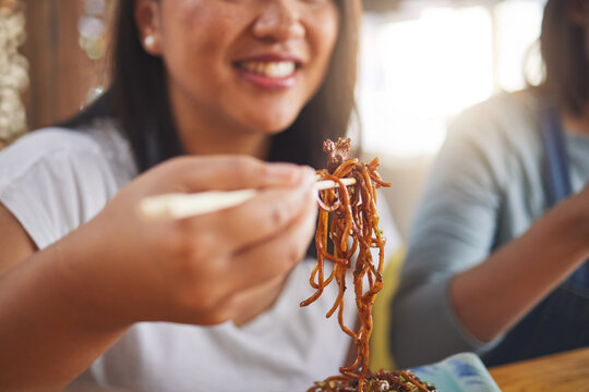 Asian, noodles and woman at a restaurant eating for dinner or lunch meal using chopsticks and happy for ramen nutrition. Plate, young and person enjoy Japanese cuisine, food or diet at a table - Powered by Adobe