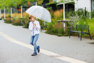 Boy holding an umbrella with raindrops. Happy little child boy having fun playing with the rain in the evening sunlight.
