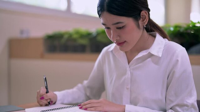 Young Asian Female student college do homework and reading a book for final exam at library, education concept.