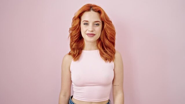 Young redhead woman smiling confident saying yes with head over isolated pink background
