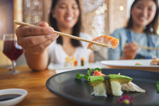 Japanese woman, chopsticks and nigiri in restaurant, smile and excited for fine dining at party. Asian friends, fish and healthy with culture, traditional and fast food in diner, sushi bar or store