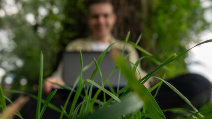 A man sits on the grass at a computer with a white screen.