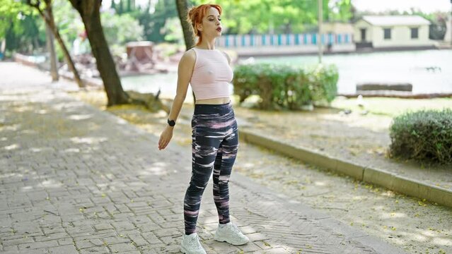 Young redhead woman wearing sportswear training legs exercise at park