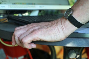 Hand von altem Mann auf rundem Tisch vor schwarzer Computertastatur und Bildschirm in garten am...