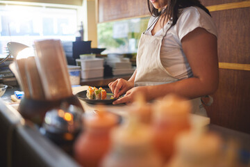 Cooking, sushi and chef with hands of person in restaurant for seafood, Japanese cuisine and nutrition. Fish, lunch and health with closeup of woman in kitchen of store for menu, takeaway and diet