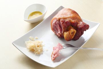 Schweinshaxe, grill pig's feet, with sauerkraut, mustard, on white plate