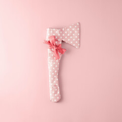 Rough axe packaged in pink polka dot gift paper with bow on pink background. Top view.