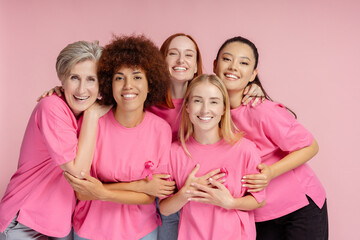 Group of smiling confident multiracial women wearing t shirts with pink ribbon looking at camera isolated on pink background. Health care, support, prevention. Breast cancer awareness month concept - obrazy, fototapety, plakaty