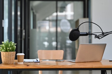 Studio podcast interior with professional condenser microphone and laptop on wooden table....
