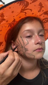 A happy family is getting ready for Halloween. A father draws a spider on a little girl's face for a holiday party. Dad and daughter are getting ready for Halloween, doing makeup. Close-up