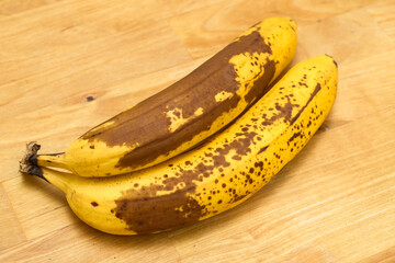 Dojrzałe banany z brązową skórką leżą na drewnianym blacie kuchennym - obrazy, fototapety, plakaty