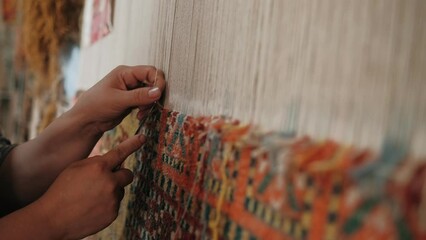 Woman weaves a traditional Arabic carpet of multicolored wool. Weaving and making handmade carpets close-up. Needlework. Handcraft - Powered by Adobe