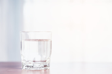 A clear glass containing water is placed upon a wooden table with soft orange sunlight from outside for the concept of healthy water consumption.