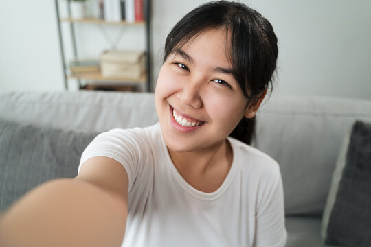 Young Asian Happy woman takes a selfie photo sitting on the sofa at home.