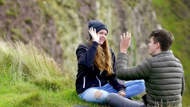 Two friends dowing high five gesture while sitting at a cliff - slow motion clip 