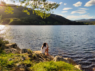 Joven sentada junto al lago de montaña al atardecer.