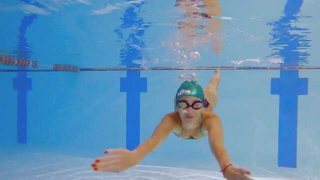 Woman athlete swims underwater in the pool. Slow motion of a female swimmer in the pool during training. The swimmer dives deep underwater.